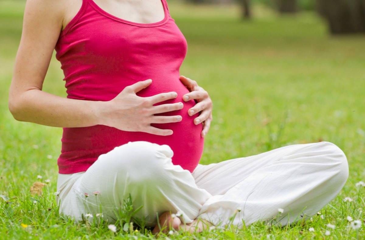 Беременная женщина сидит на траве