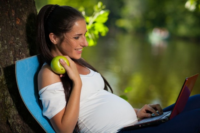 Беременная женщина сидит в парке